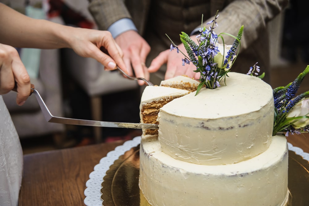 Bride and groom cutting a three-tier wedding cake with silver knife during their reception