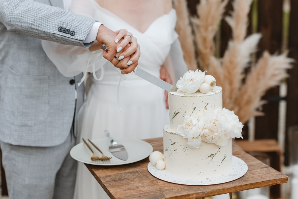 Bride and groom cutting a three-tier wedding cake with silver knife during their reception