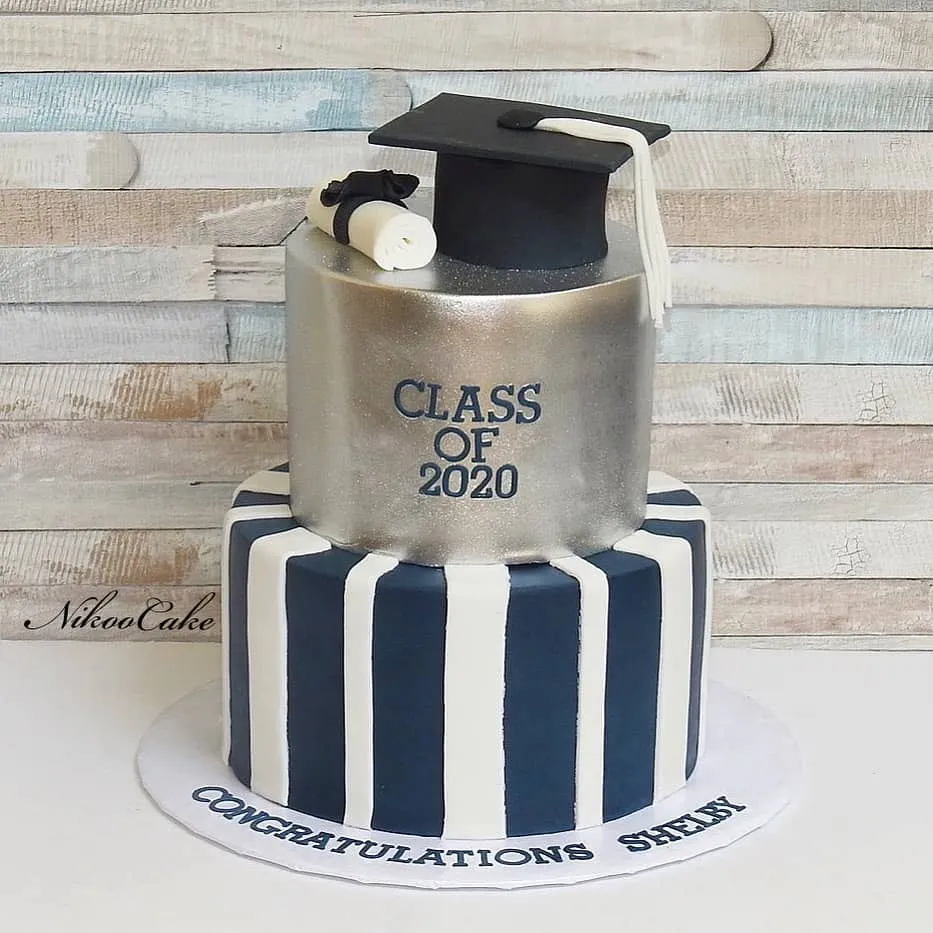 Silver, navy and white two-tier graduation cake with a fondant cap, diploma and “Class of 2020” decoration.
