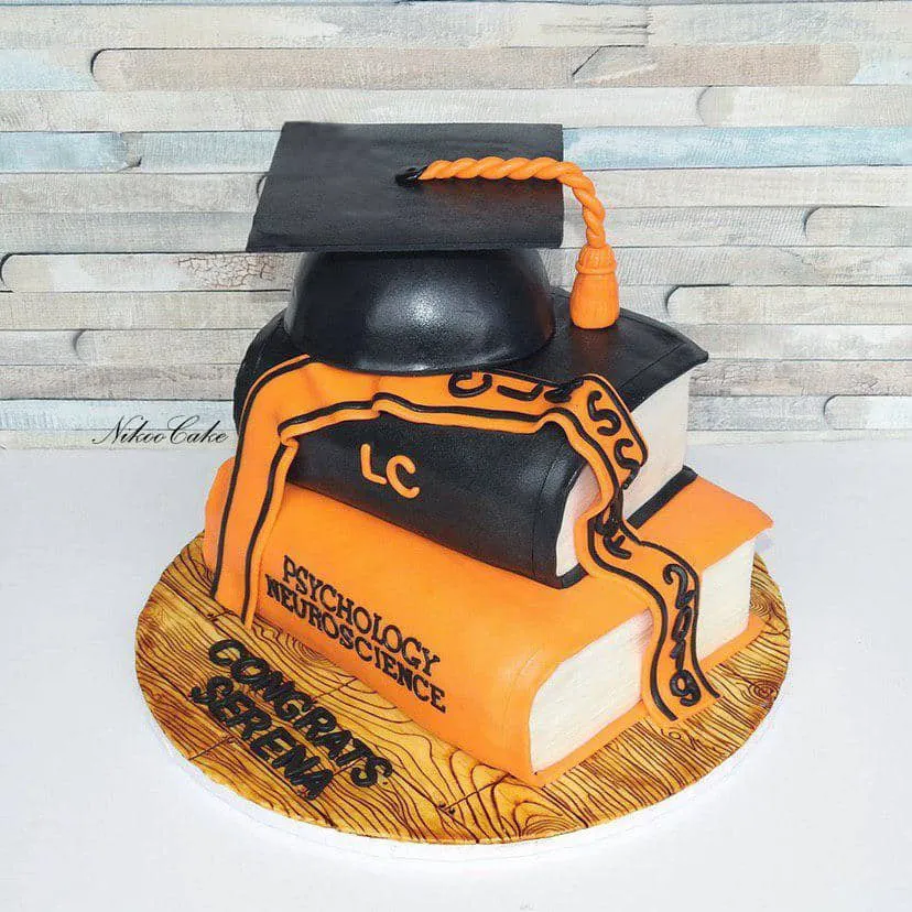 Orange and black psychology and neuroscience graduation cake shaped like textbooks with a fondant cap and tassel.